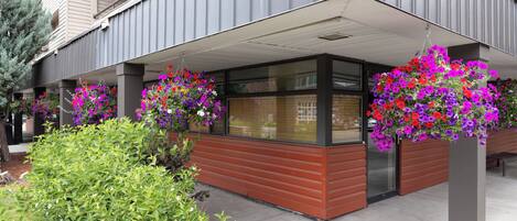 A modern building with a covered entrance area, large windows, and hanging flower baskets.