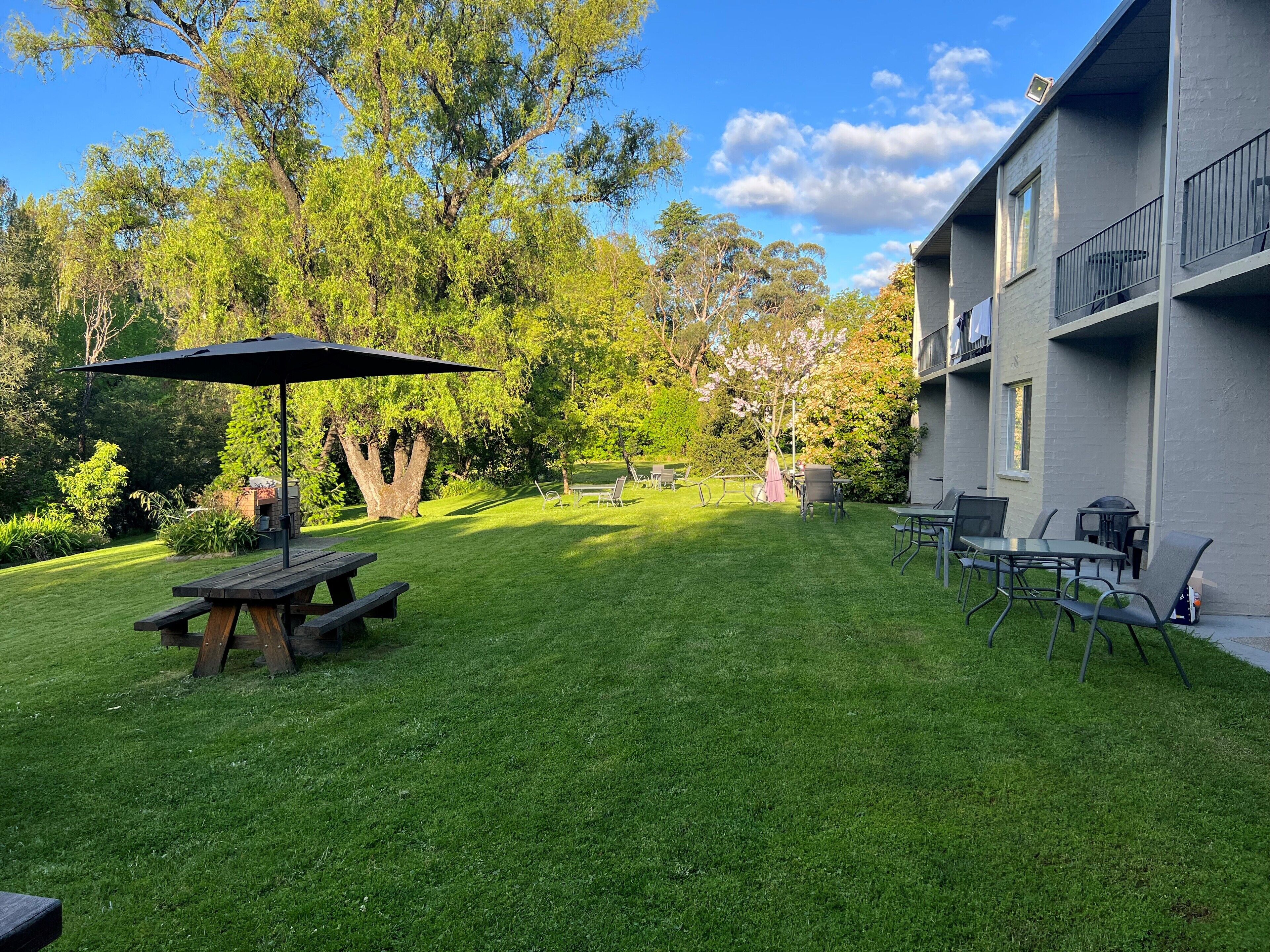 Un patio trasero bien cuidado con una mesa de picnic, asientos exteriores y un paraguas grande.