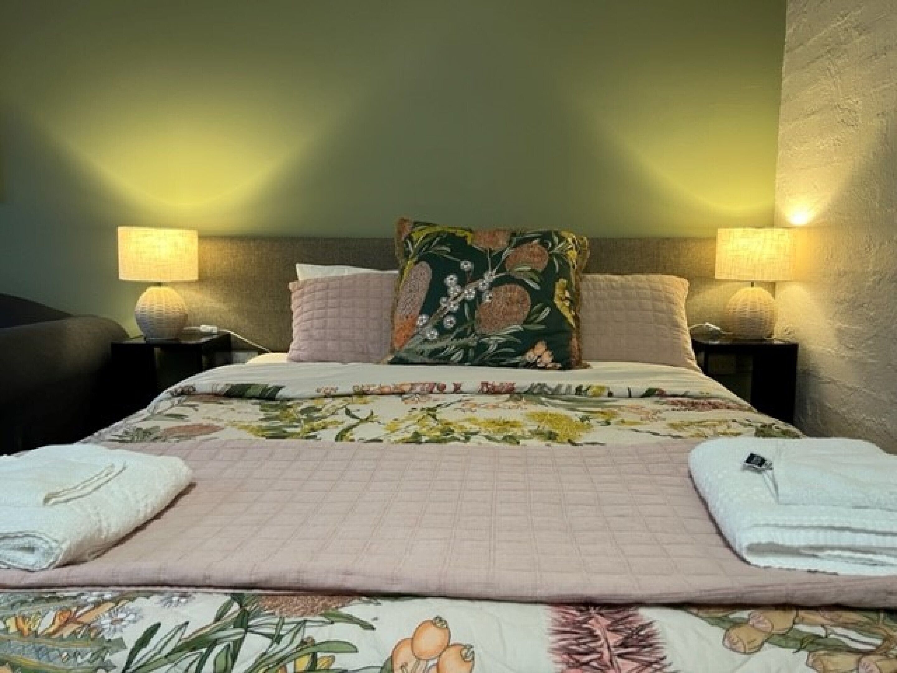 A neatly made bed with floral bedding, two bedside lamps, and a headboard.