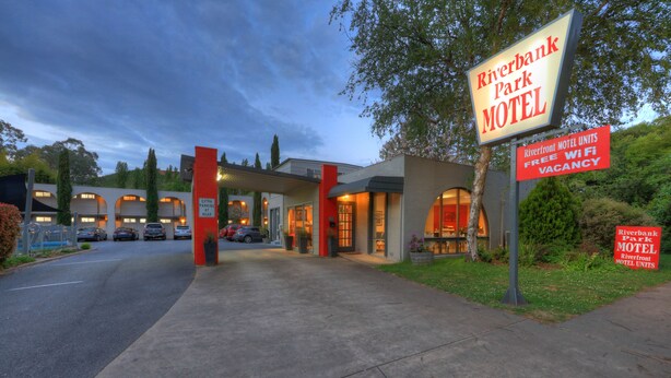 A Riverbank Park Motel with a modern design, featuring a prominent entrance, visible parking area, and signs indicating extra parking and WiFi availability. - Riverbank Park Motel (Bright)
