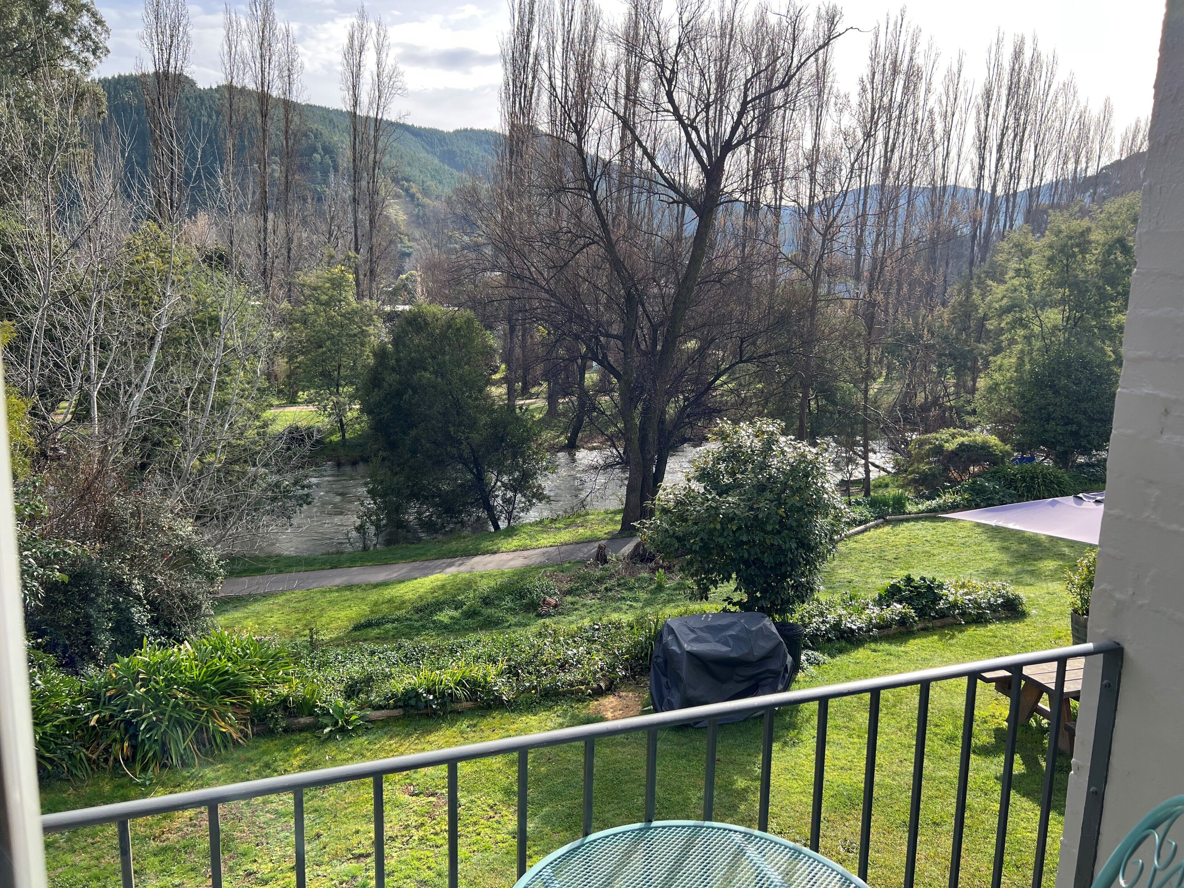 A balcony with a view of a landscaped garden, a covered grill, and a metal railing.