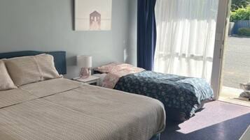 Un dormitorio con dos camas, una mesita de noche, una ventana con cortinas y una puerta que da al exterior.