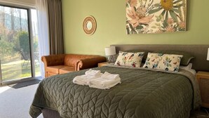 A bedroom with a large bed, a sofa, a round mirror, and a floral painting. - Riverbank Park Motel (Bright)