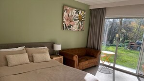 A bedroom with a large bed, a sofa, a painting on the wall, and a view of the outdoors through a glass door. - Riverbank Park Motel (Bright)