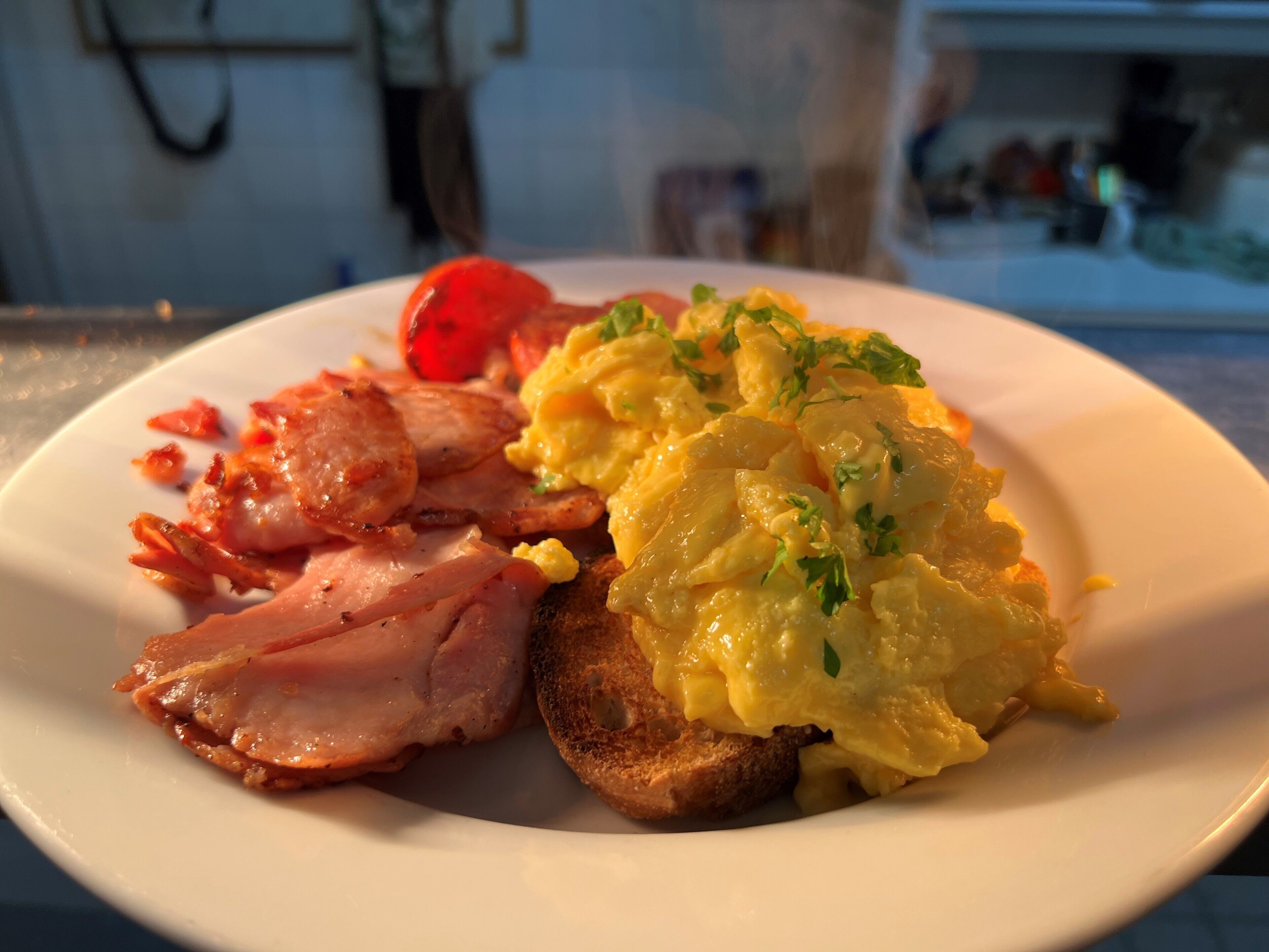 Un plato de desayuno con huevos revueltos, tocino, tostadas y tomate.