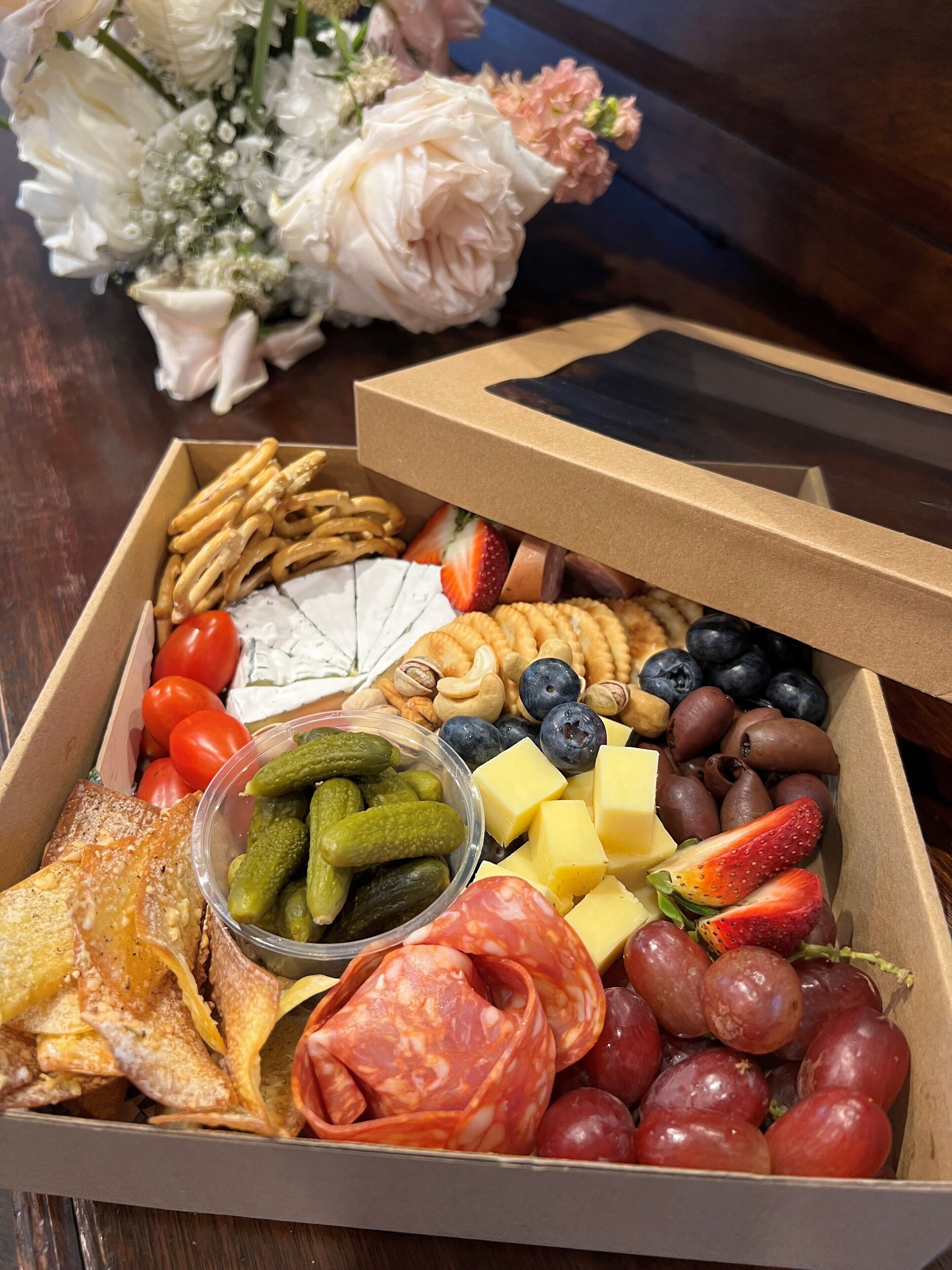 A box of assorted snacks and fruits including pretzels, cheese, grapes, and strawberries.