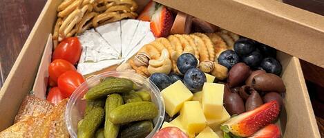A box of assorted snacks and fruits including pretzels, cheese, grapes, and strawberries.
