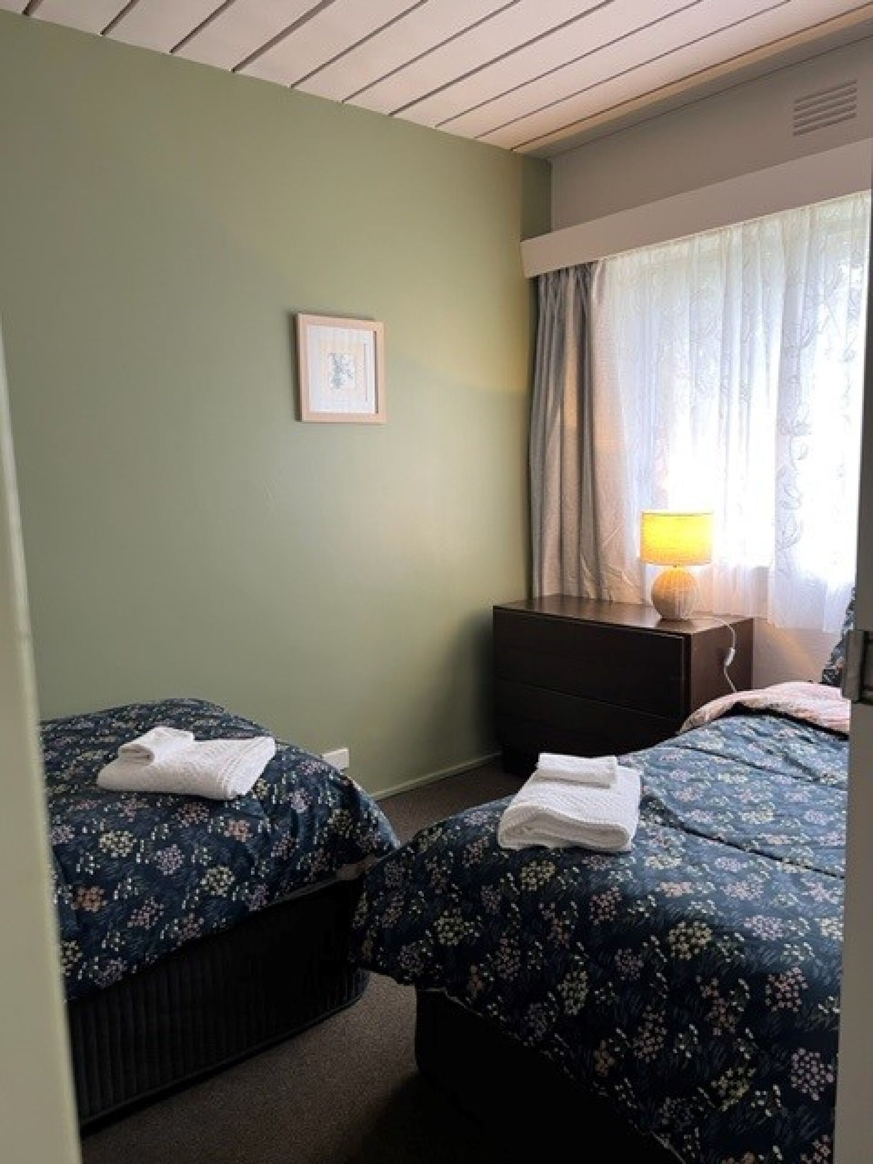 A hotel room with two beds, a nightstand, a lamp, and a framed picture on the wall.