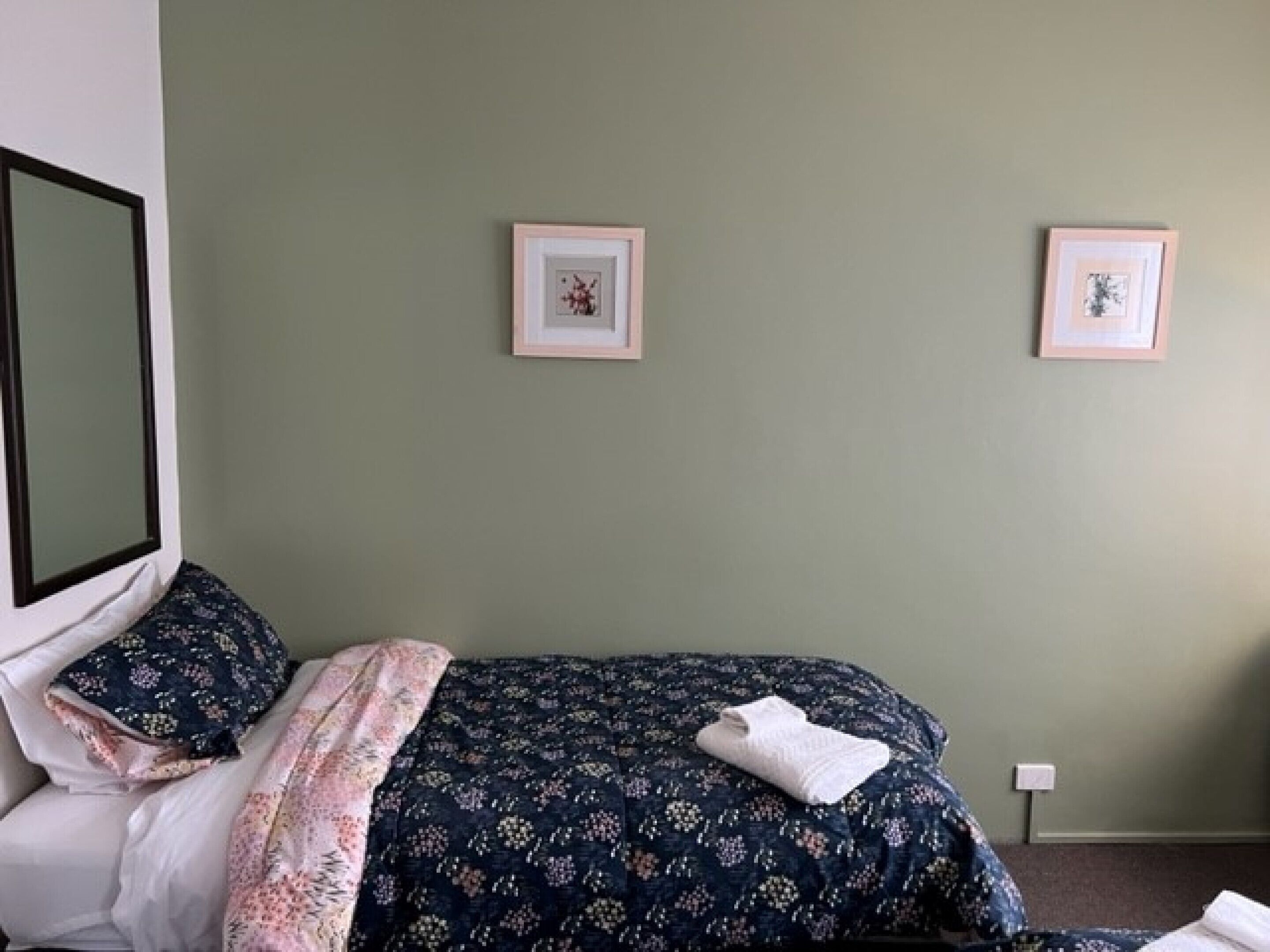 Een slaapkamer met een bed, kussens, een deken en twee afbeeldingen in lijsten aan de muur.