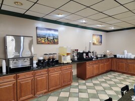 A hotel kitchen with a coffee station, whole milk and skim milk dispensers, a coffee maker, and a food display.