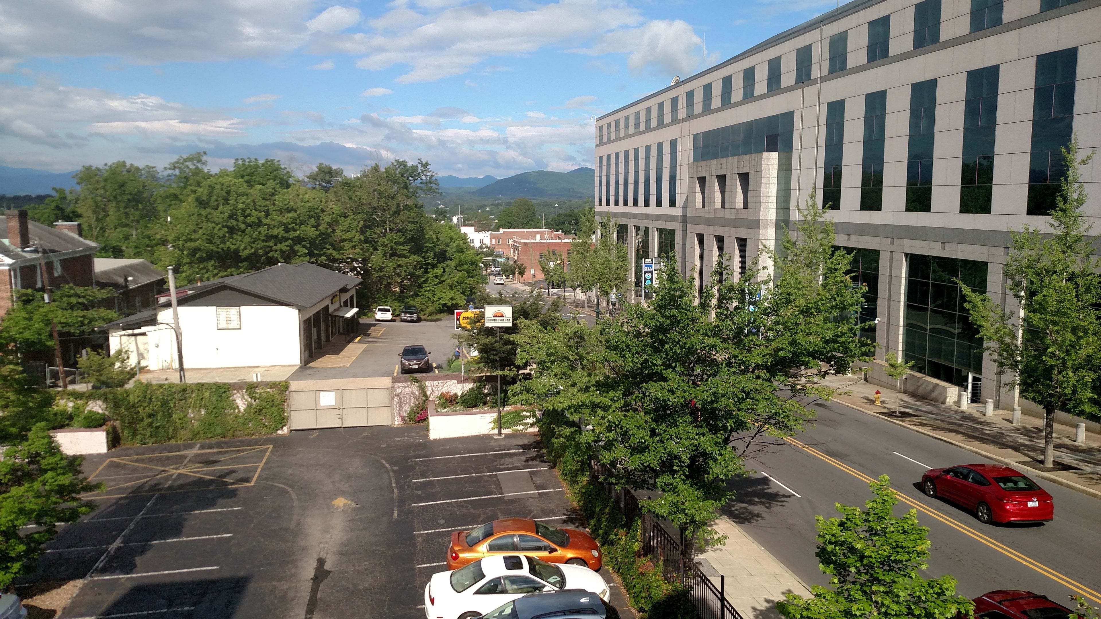 A parking lot with several cars, a building with large windows, and a view of mountains in the background.