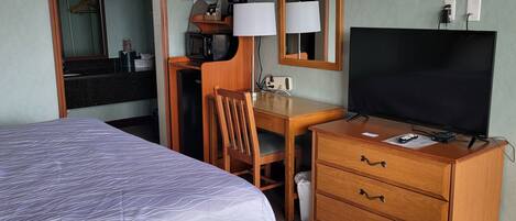 A hotel room with a bed, a desk with a chair, a television, and a dresser.