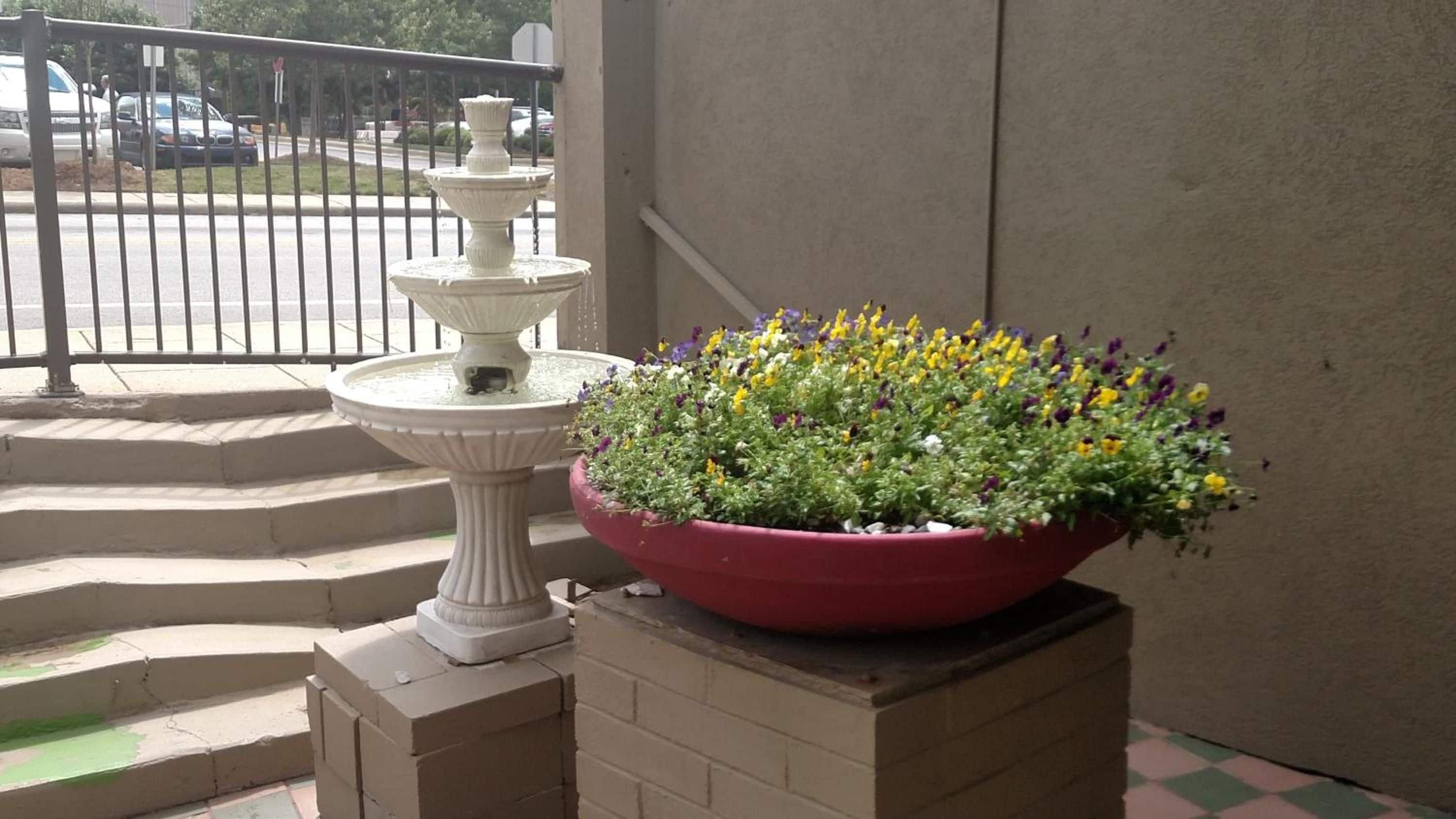 Une fontaine d’extérieur blanche et un grand pot de fleurs ornant un balcon.