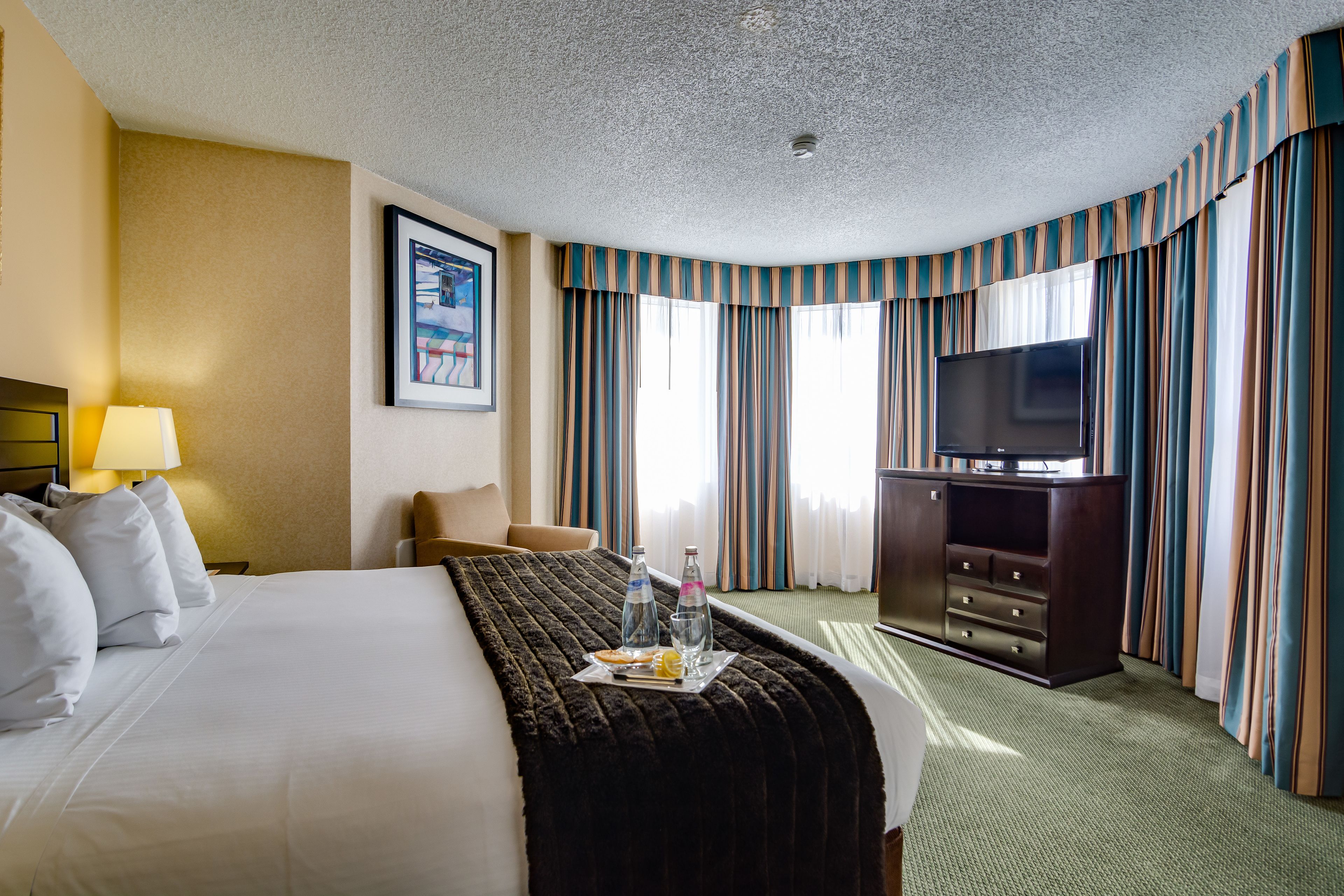 A hotel room with a large bed, a flat-screen TV, a desk with a lamp, and a minibar.