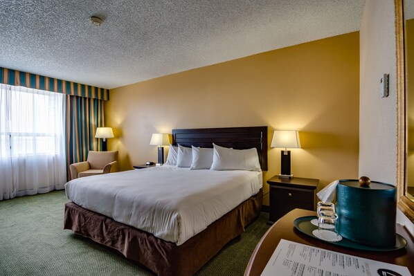 A hotel room with a large bed, two bedside tables with lamps, a chair, a mirror, and a green carpet.