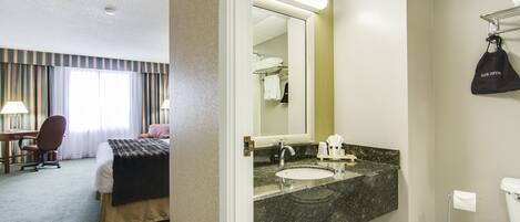 Habitación de hotel con cama, escritorio, silla y baño con lavamanos, espejo e inodoro.