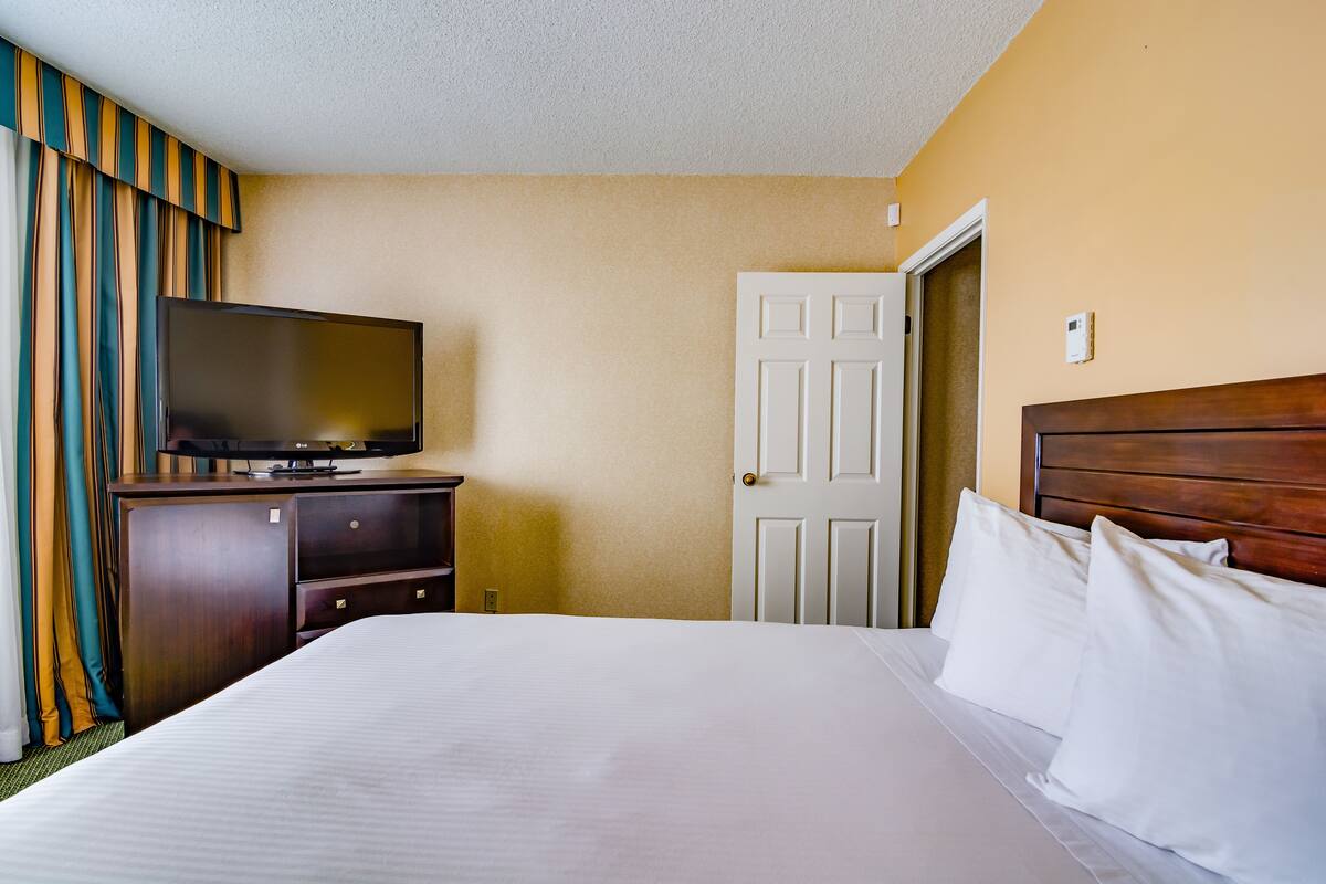 Une chambre d’hôtel avec un lit, un téléviseur posé sur une commode en bois et une porte.