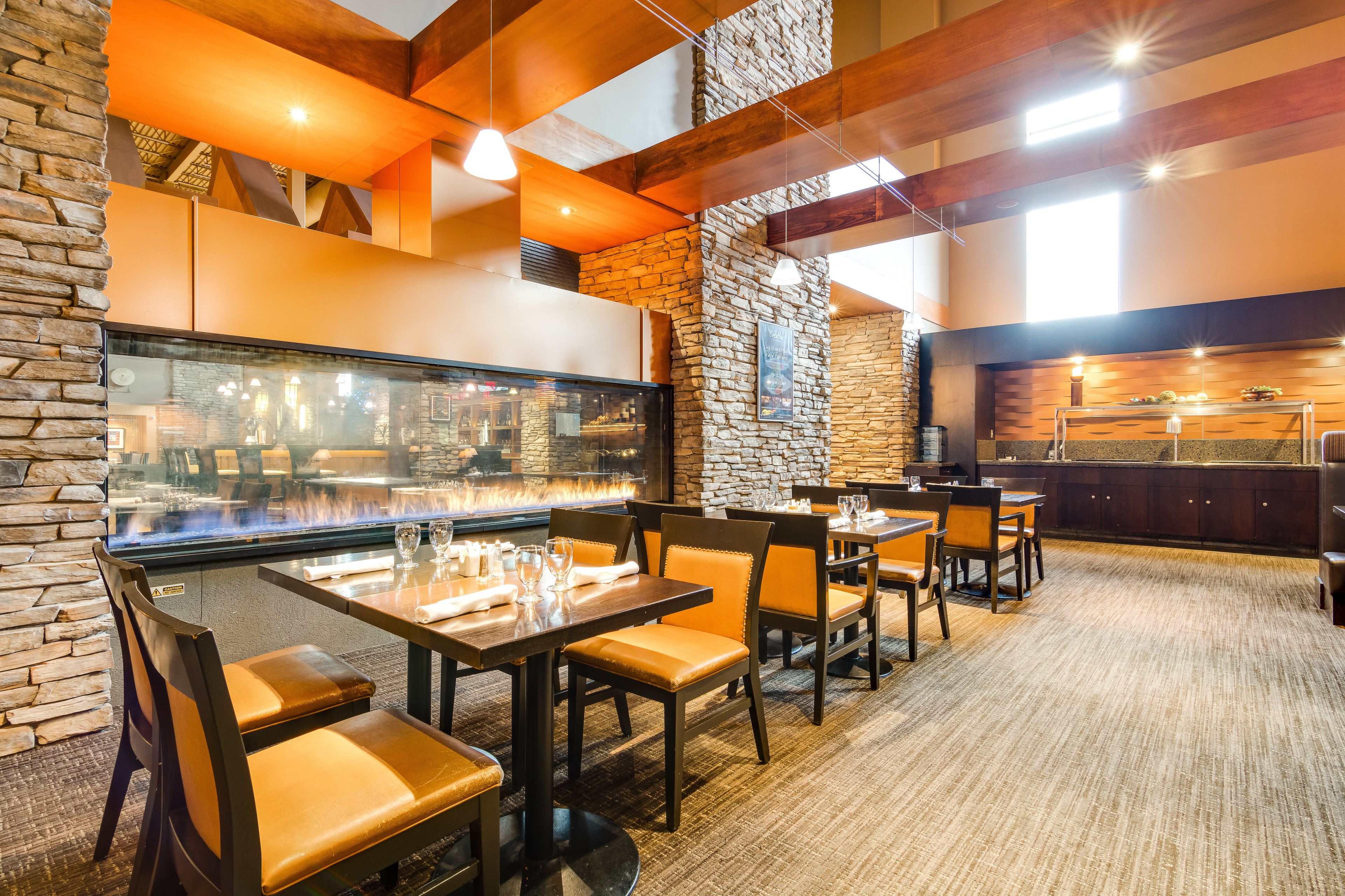 A restaurant with stone walls, wooden beams, and a fireplace. Tables and chairs are arranged for dining.