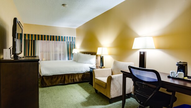 A hotel room with a bed, desk, chair, lamps, and a coffee maker.