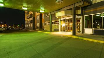A building with a covered entrance, large windows, and a parking area at night.
