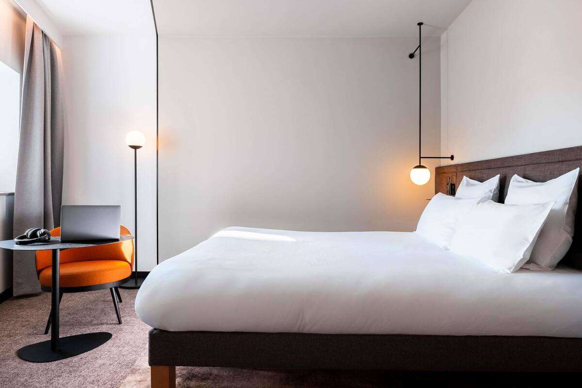 Ein modernes Hotelzimmer mit einem großen Bett, einem Schreibtisch mit einem Laptop und einem Sessel.