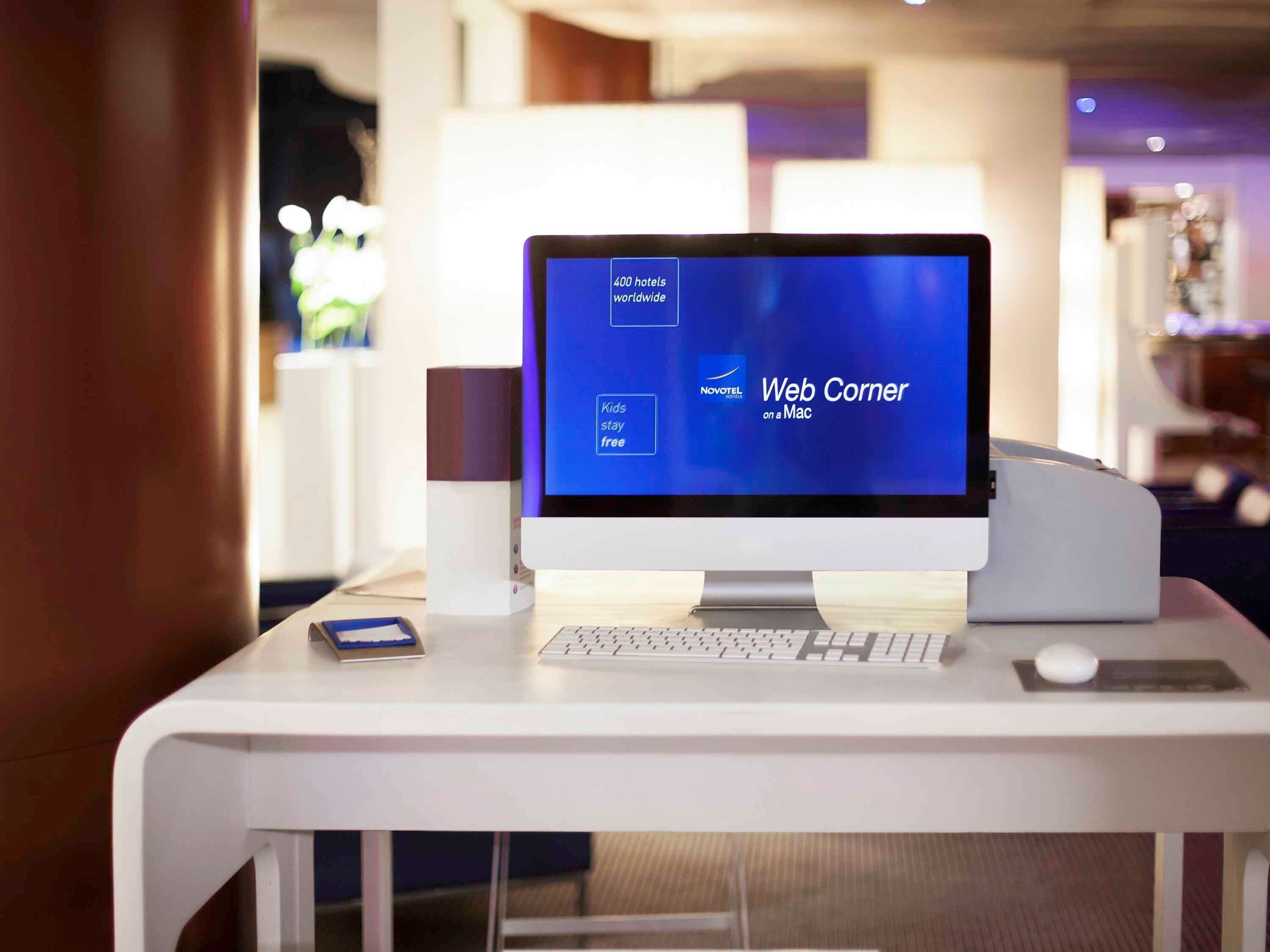 A hotel reception desk with a computer monitor displaying a Novotel website, a keyboard, a mouse, and a small blue card.