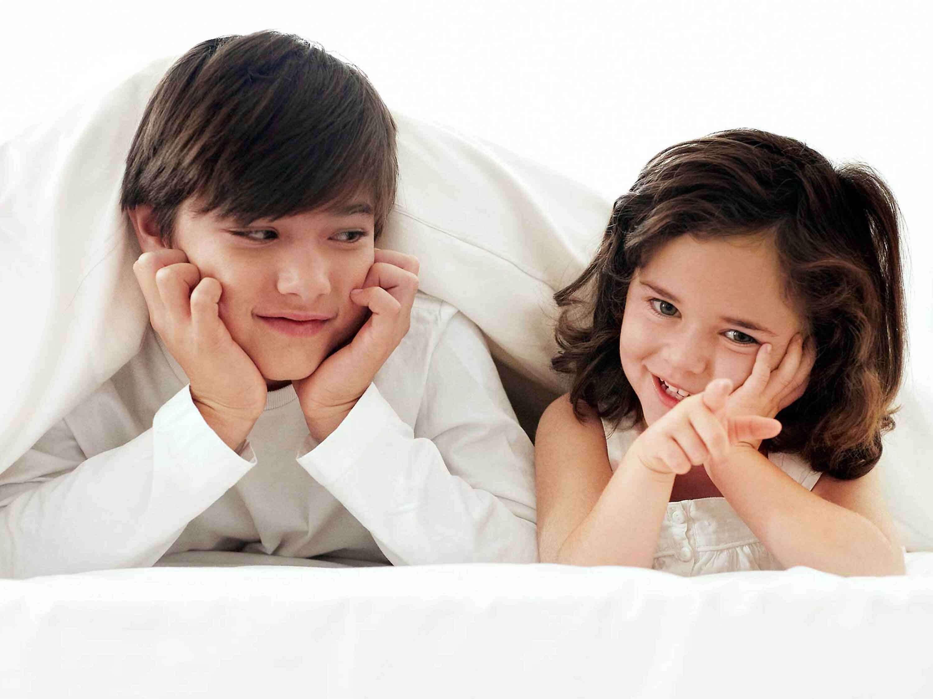 Un niño y un adulto recostados en la cama, cubiertos por una manta blanca.