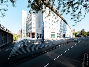 A modern hotel with a prominent entrance, a staircase leading to the lobby, and a clear view of the street.
