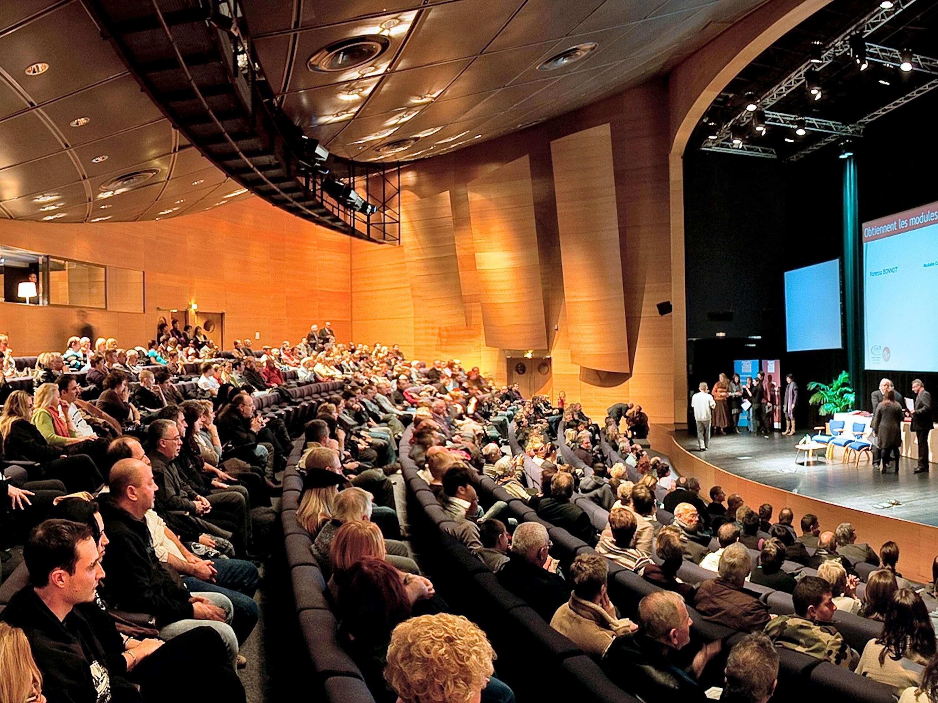 A large auditorium with tiered seating, a stage, and a presentation screen.