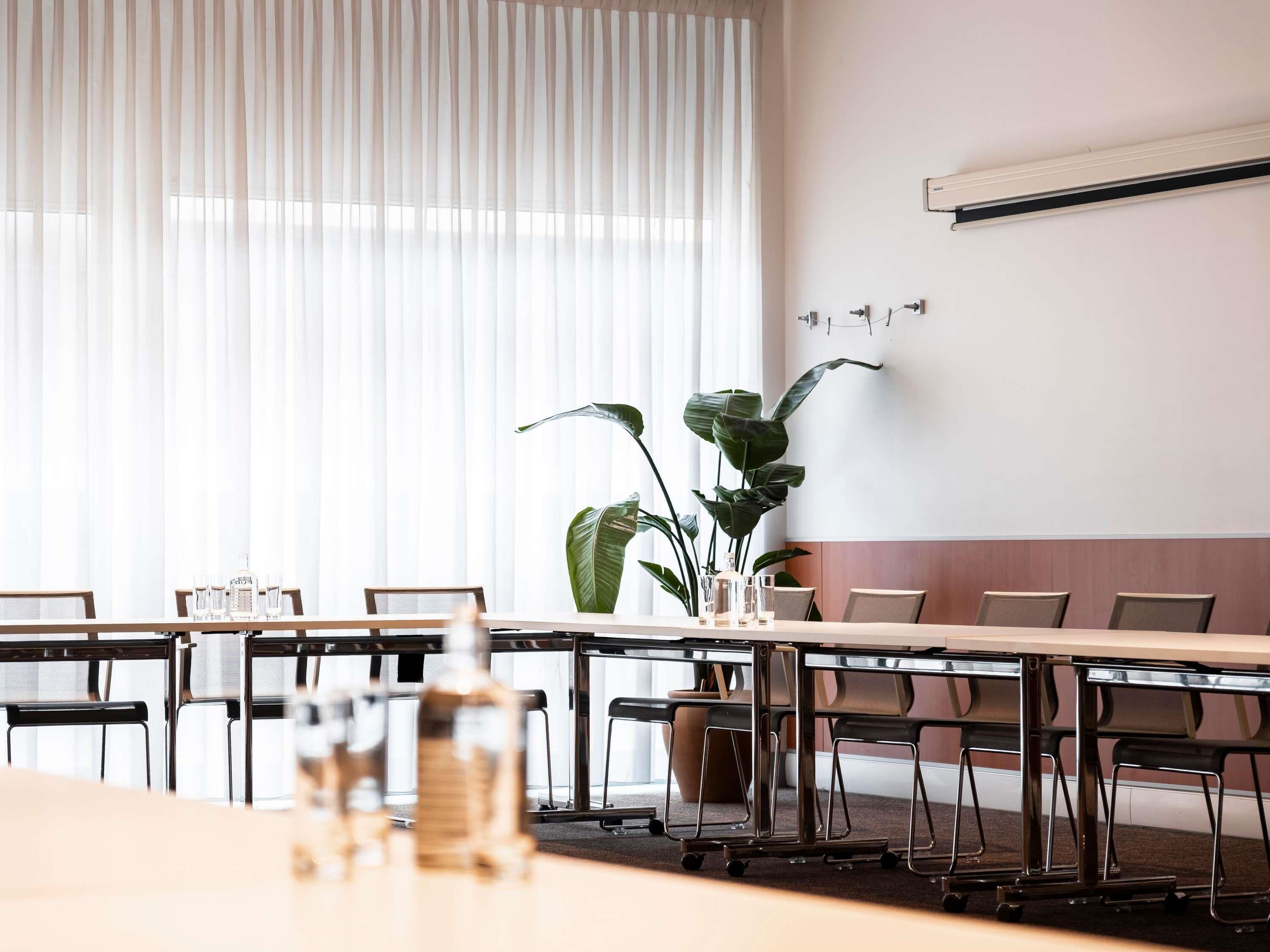 Une salle de conférence avec une longue table, des chaises, une plante en pot et un climatiseur fixé au mur.