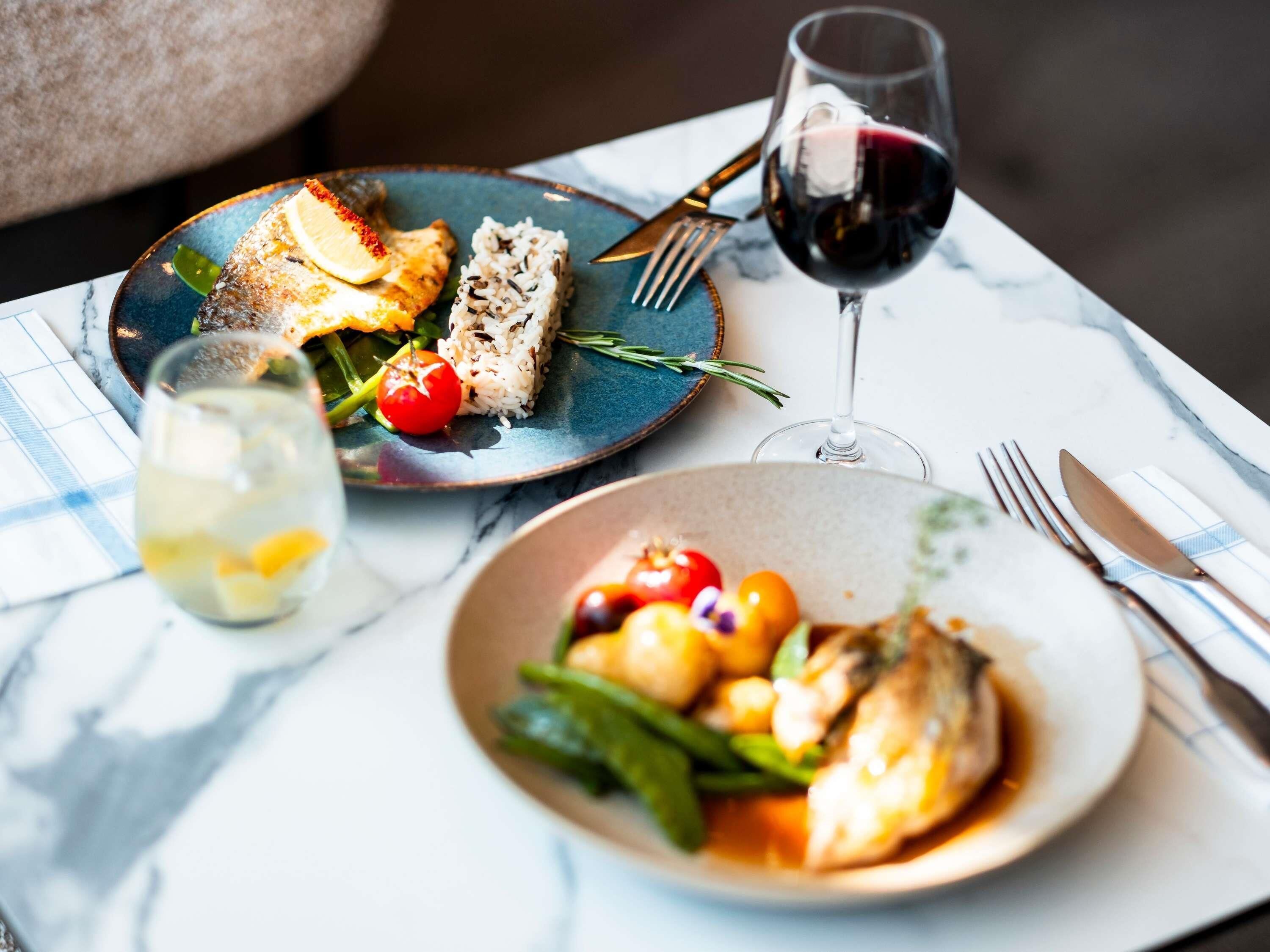 Une table avec des assiettes de nourriture, un verre de vin rouge et un verre d’eau.