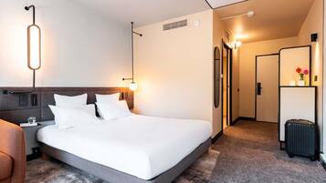 Una habitación de hotel moderna con una cama grande, mesitas de noche, un armario y un baño visible a través de una puerta abierta.