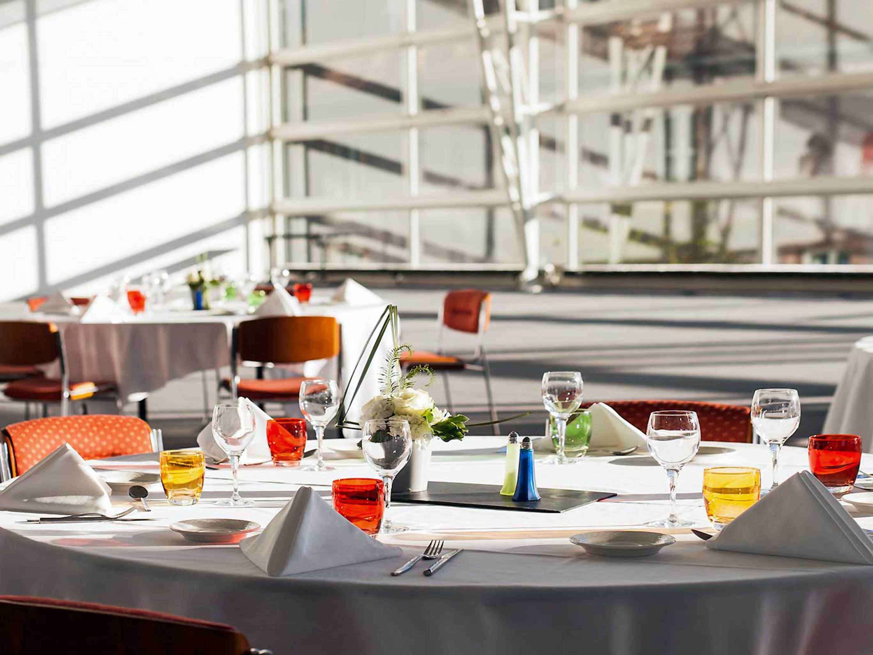 A restaurant setting with tables set for dining, featuring a modern interior with glass partitions and a view of the outside.