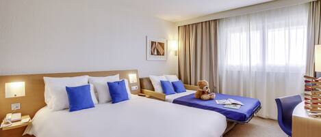 Habitación de hotel con dos camas, un escritorio, una silla y un osito de peluche.