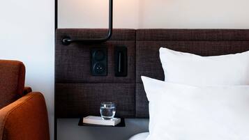A neatly arranged hotel room with a bed, a bedside table with a book and glass of water, a lamp, and a chair.
