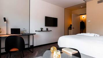Una habitación de hotel moderna con cama, escritorio, silla y una pequeña mesa con una bebida y un libro.