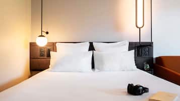 Una cama bien hecha con sábanas blancas, un par de auriculares y un libro sobre la mesita de noche.