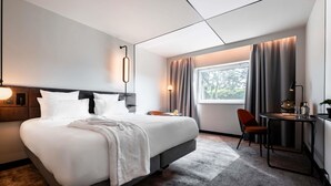 Une chambre d’hôtel moderne avec un grand lit, un bureau et une fenêtre avec des rideaux.