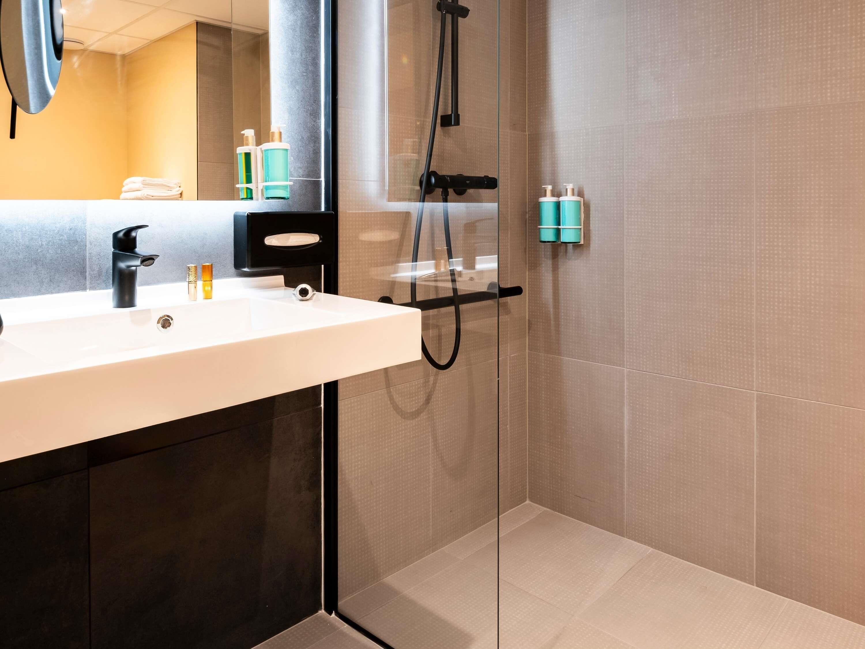 A modern bathroom with a white sink, black faucet, and a glass shower enclosure.