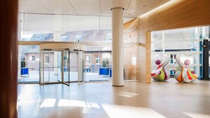 Un hall d’entrée spacieux, doté d’une entrée en verre, d’une grande colonne et offrant une vue sur les bâtiments environnants.