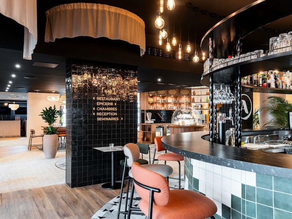 A modern bar area with a black tiled wall, a wooden reception desk, and a bar counter with various bottles and glasses.