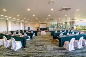 Un salón de conferencias con varias mesas y sillas, piso alfombrado y vistas al exterior.