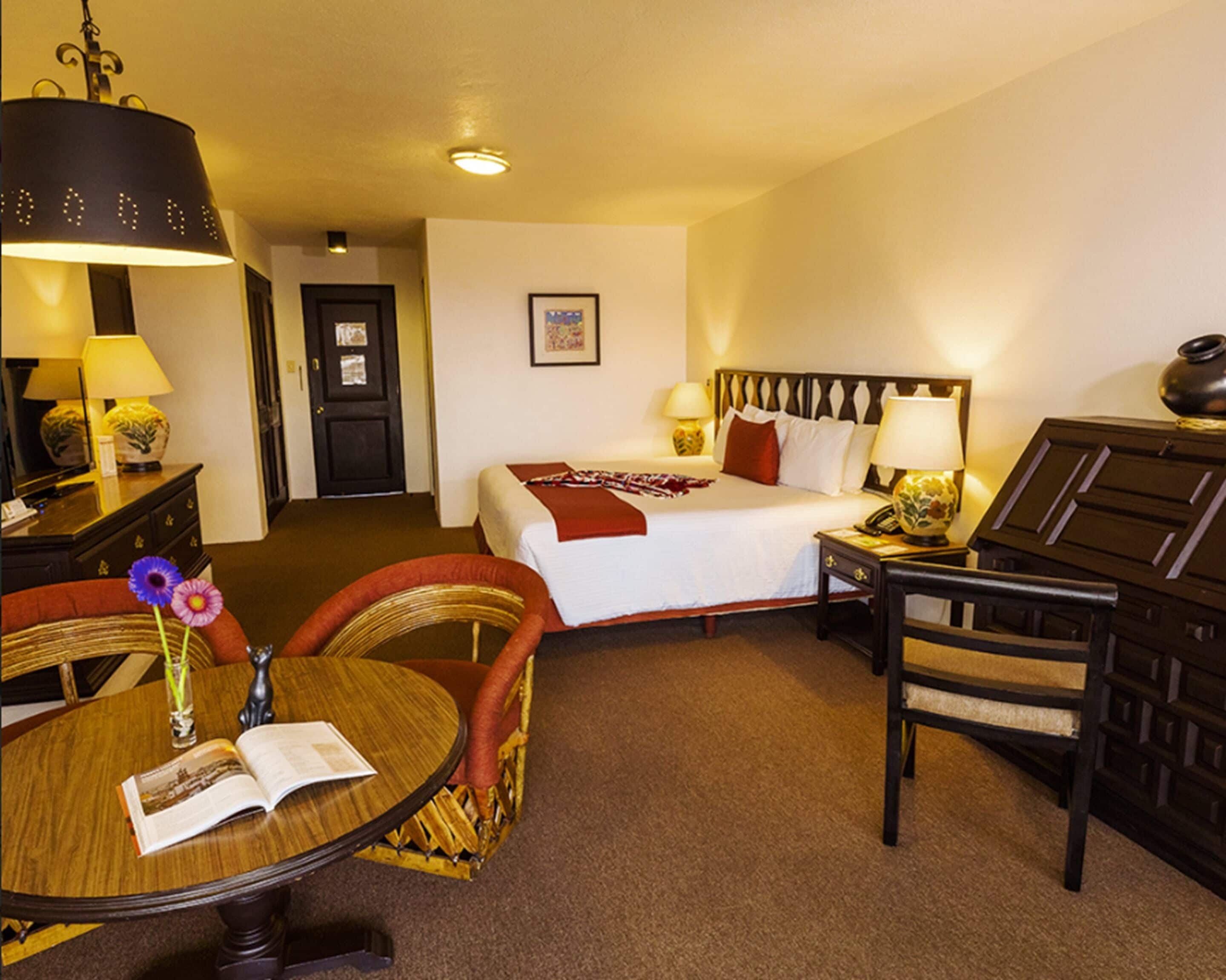 A hotel room with a bed, bedside tables, a chair, a round table with a book, and a lamp.