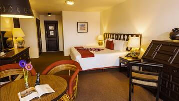 A hotel room with a bed, bedside tables, a chair, a round table with a book, and a lamp.