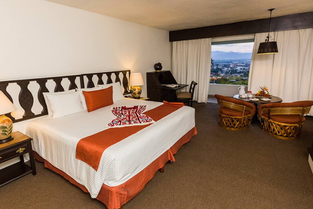 Una habitación de hotel con una cama grande, un escritorio, una silla y vistas a un paisaje urbano.