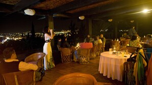 An outdoor dining area with round tables and wicker chairs, overlooking a cityscape at night. - Hotel Victoria Oaxaca (Oaxaca)