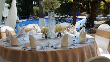 Una mesa redonda dispuesta para un evento formal, con mantel color beige, servilletas blancas y cubiertos.