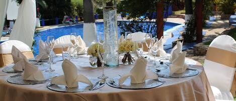 Una mesa redonda dispuesta para un evento formal, con mantel color beige, servilletas blancas y cubiertos.