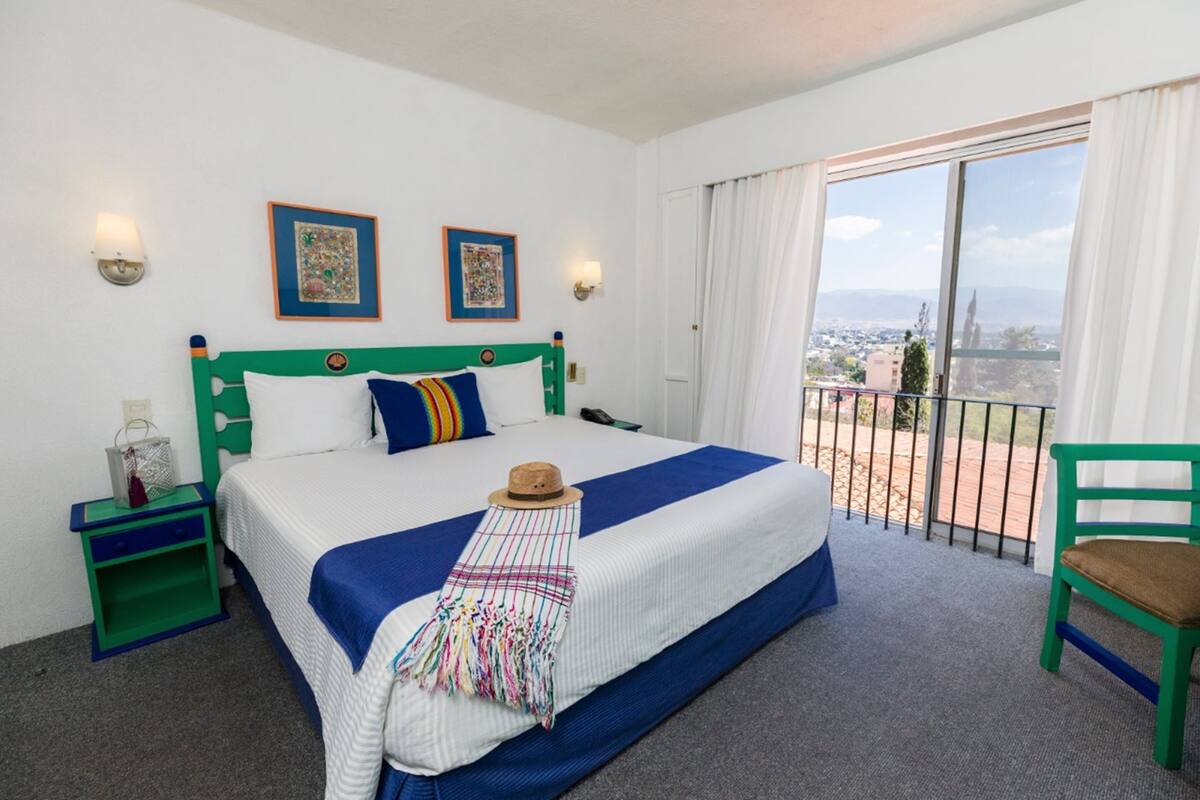 Una habitación de hotel con una cama grande, un balcón con vistas y una silla verde.
