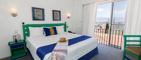 Een hotelkamer met een groot bed, een balkon met uitzicht en een groene stoel.